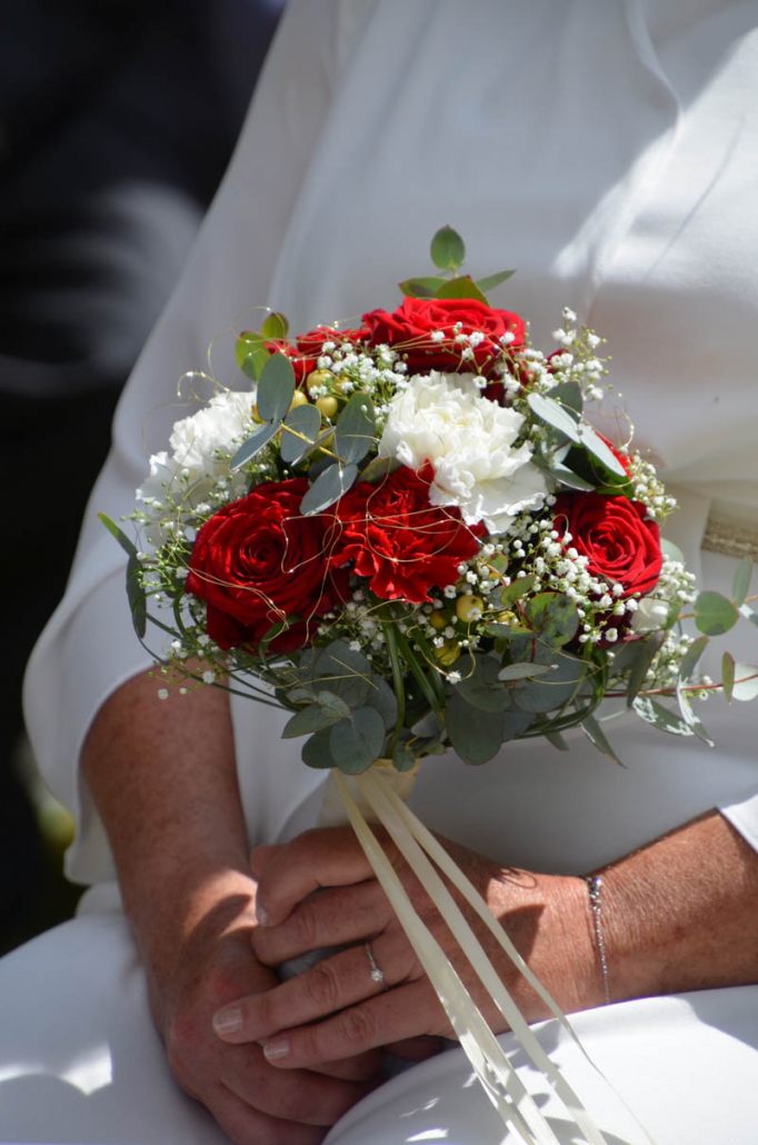 sitzende Braut hält Brautstrauß mit roten und weißen Rosen