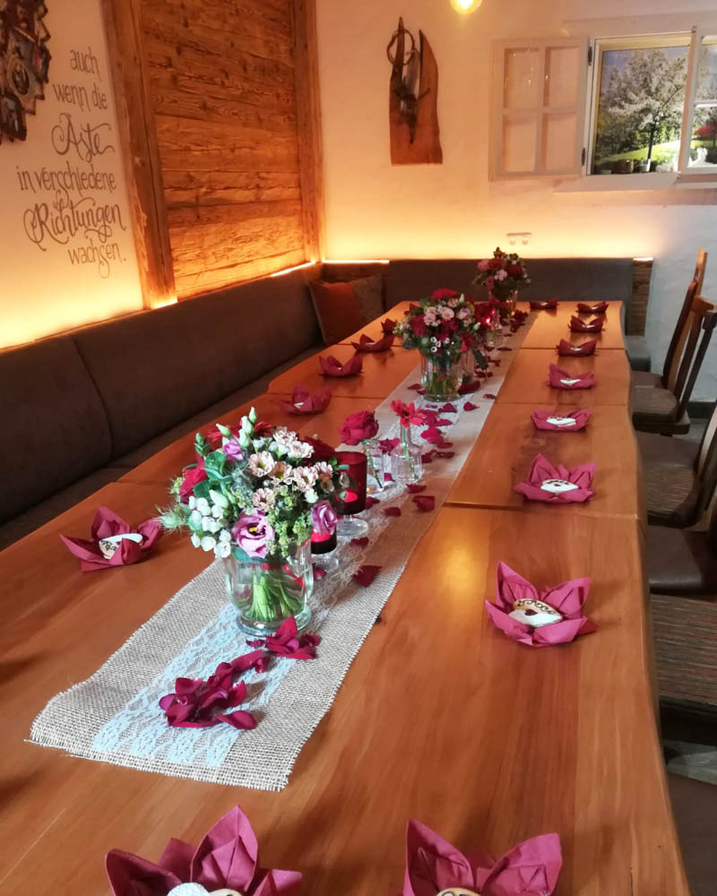 lila Tischdekoration, 3 rote-weiße Blumensträuße und Rosenblätter in der Mitte des Tisches