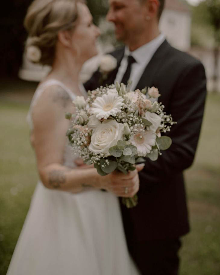 weißer Blumenstrauß mit Ehepaar im Hintergrund