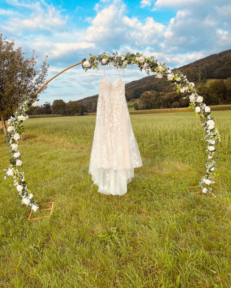 Brautkleid hängt am großen Rosenbogen, mit weißen Blumen geschmückt
