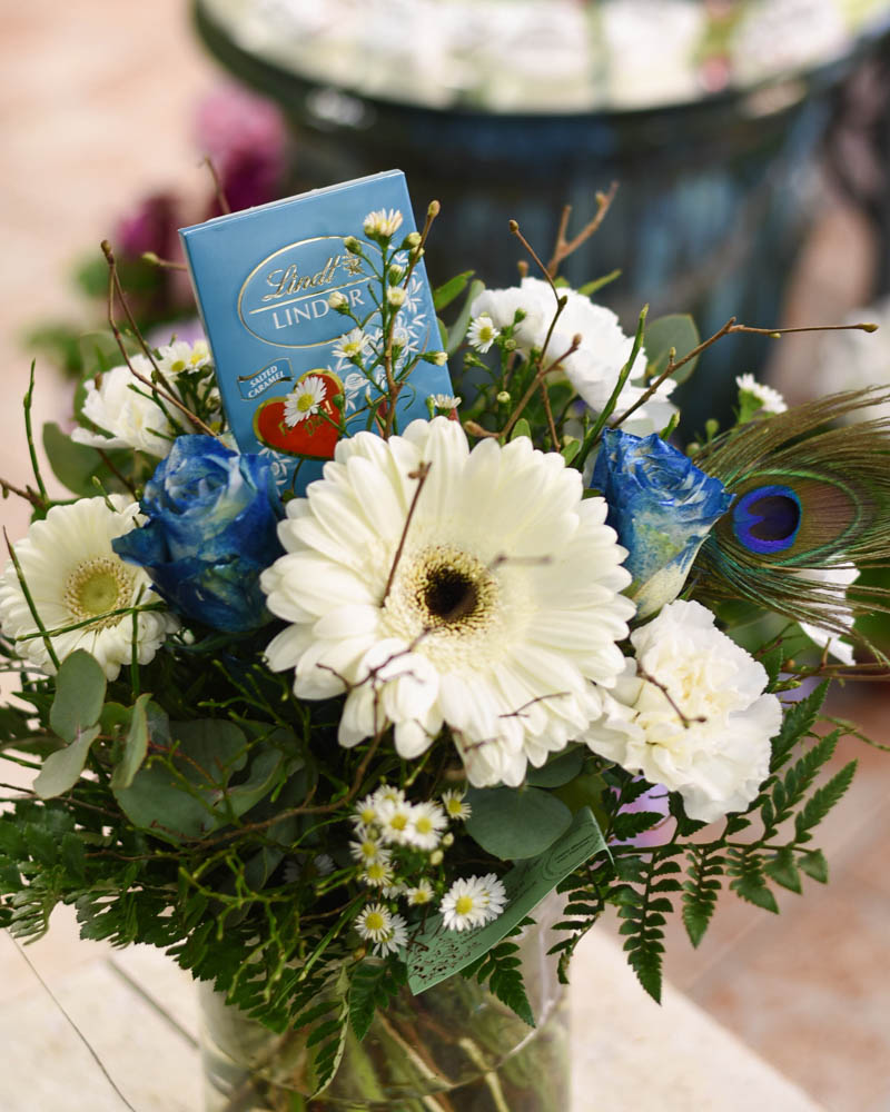 weißer Blumenstrauß mit blauen Rosen und Lindt Schokoladentafel in der Mitte